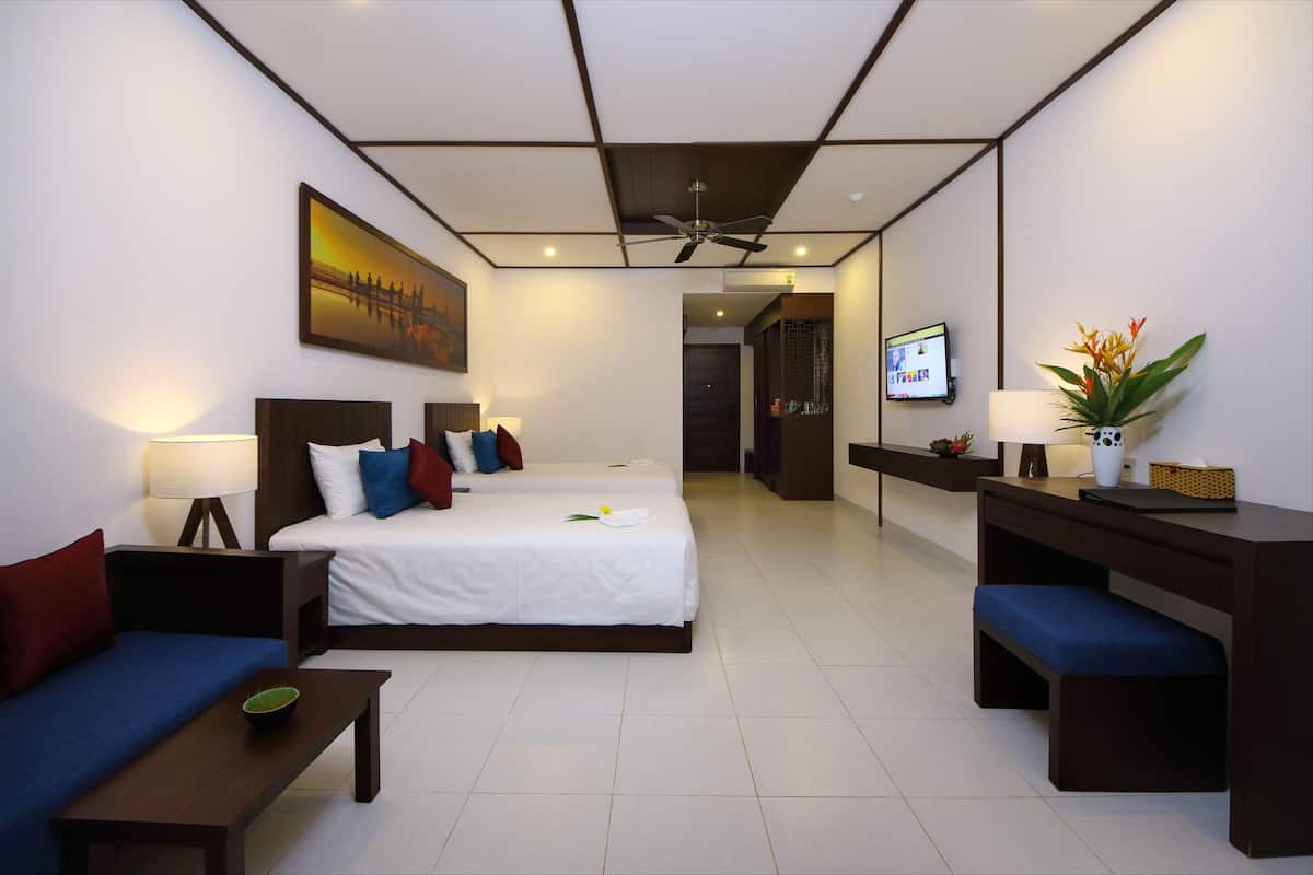 A hotel room with a bed, a desk, a chair, a sofa, a TV, and a ceiling fan.