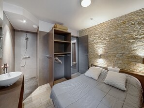 A modern bedroom with a large bed, a walk-in closet, a bathroom with a shower, and a stone accent wall.