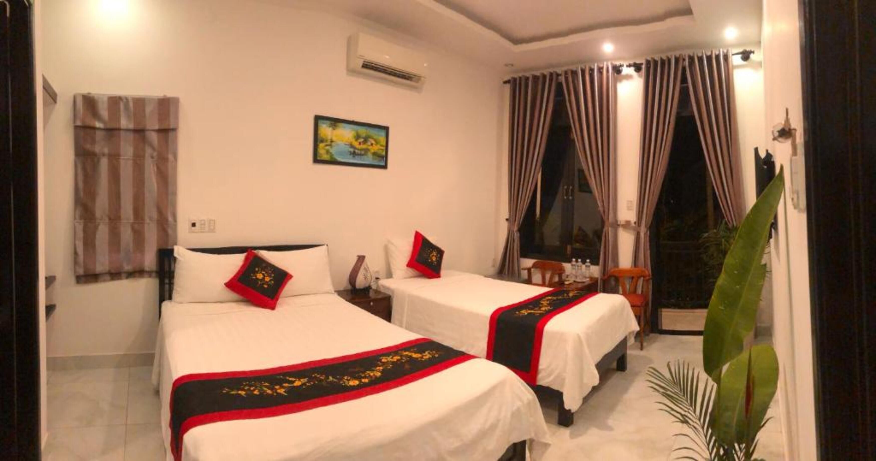 A hotel room with two beds, a painting on the wall, an air conditioner, and a window with curtains.