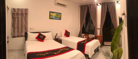 A hotel room with two beds, a painting on the wall, an air conditioner, and a window with curtains.