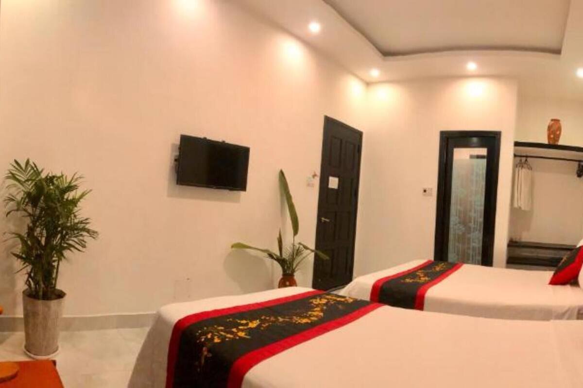 Habitación de hotel con dos camas, un televisor de pantalla plana, una puerta y una planta en maceta.