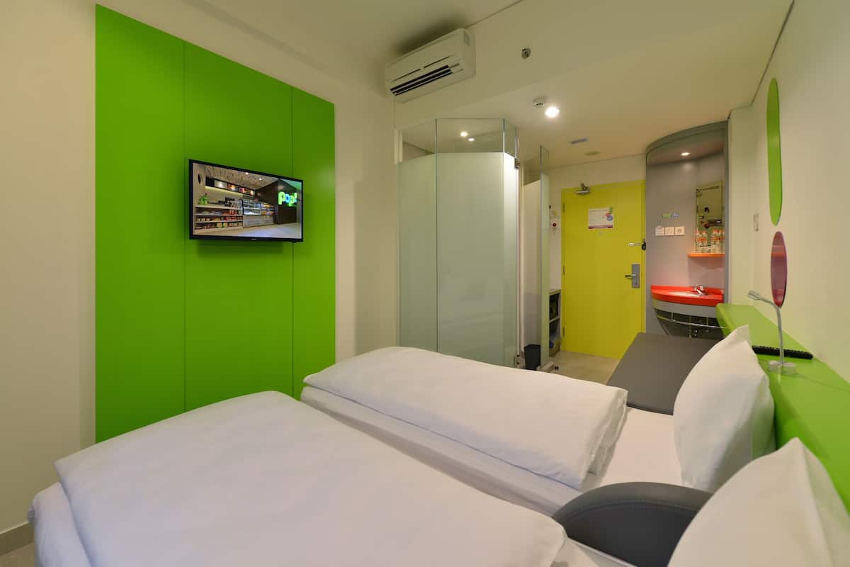 A hotel room with two beds, a television, a glass partition, and a bathroom with a yellow door.