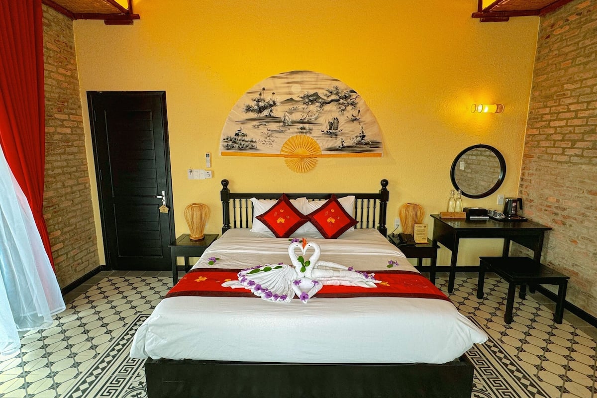 A hotel room with a bed, a wall-mounted painting, a mirror, and a small table.