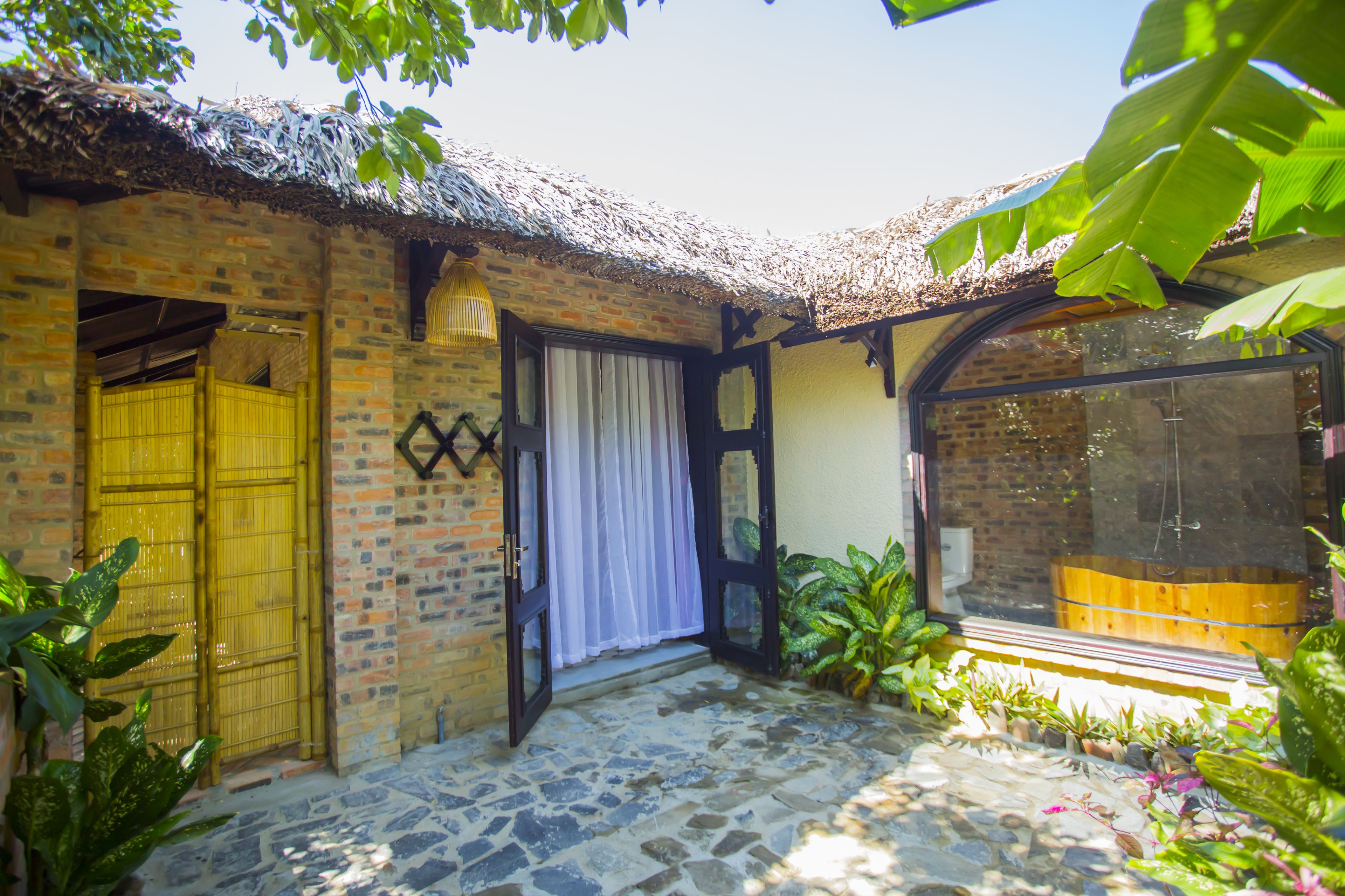 A brick building with a thatched roof, a wooden door, and a window with a curtain.