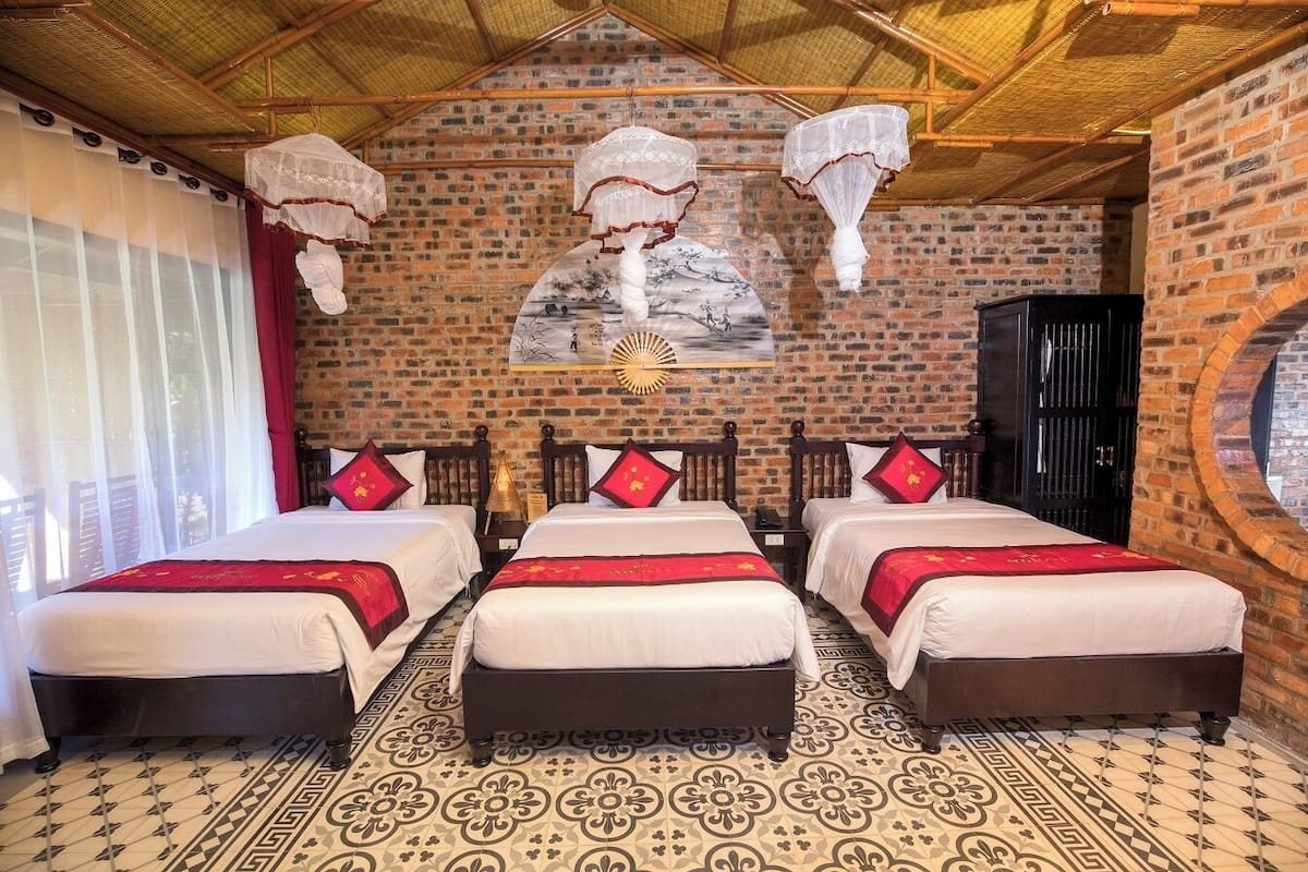 A hotel room with three beds, a brick wall, and a patterned floor.