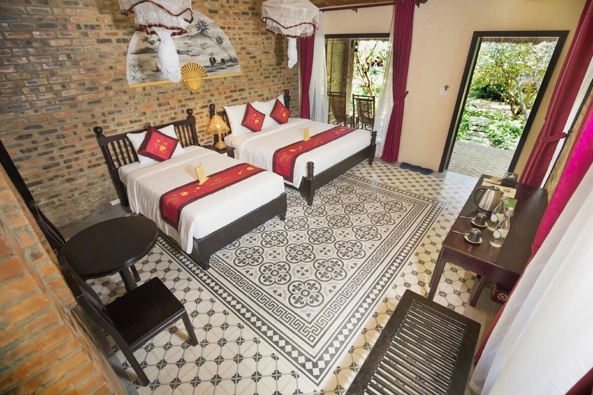 Quarto de hotel com duas camas, uma mesinha e vista para o exterior.