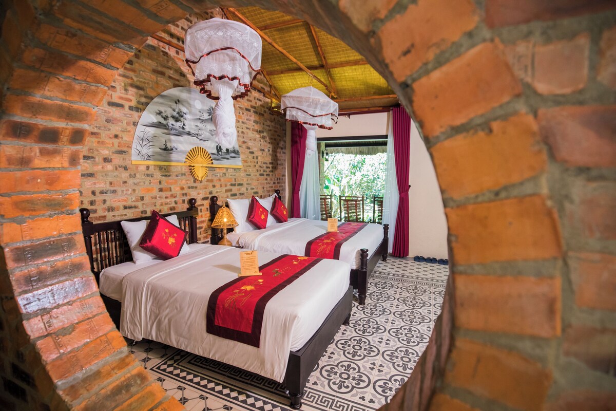 Una habitación tradicional con pared de ladrillo, dos camas con ropa de cama roja y blanca, suelo estampado y faroles colgantes.