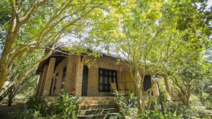 A rustic brick building with a thatched roof, surrounded by lush greenery and trees. - Hue Ecolodge (Hue)