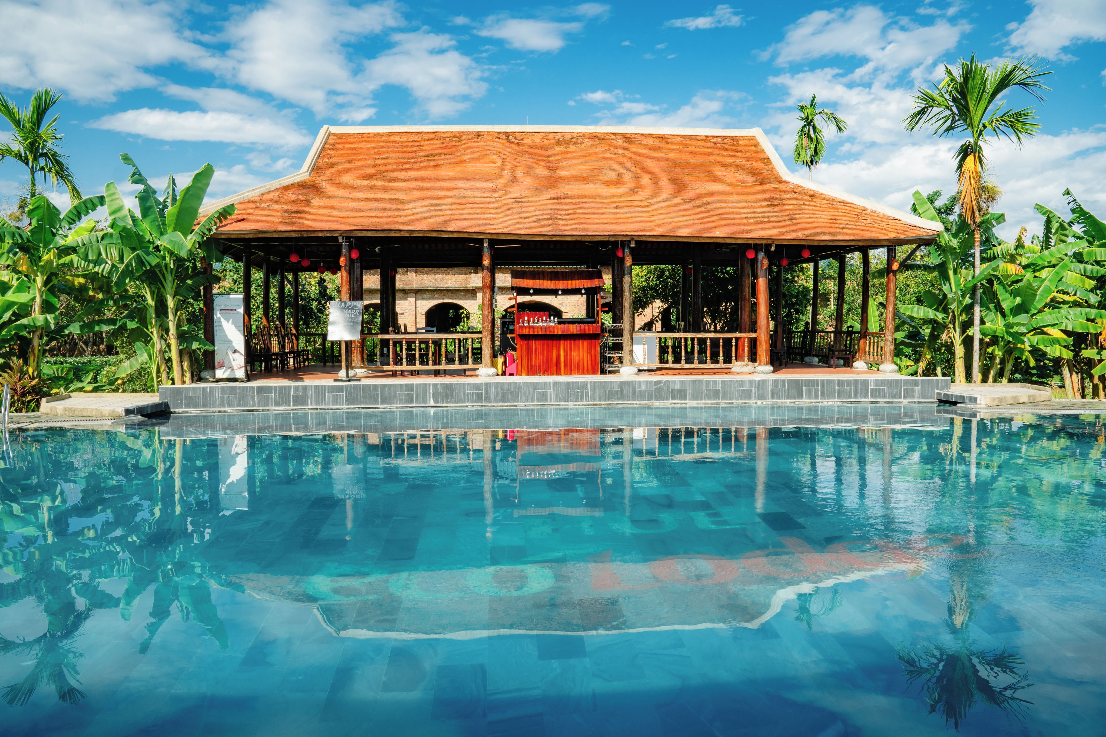 A pool with a covered area and a building with a tiled roof.
