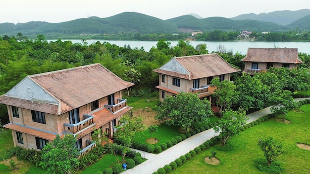 A bungalow with a tiled roof, a balcony, and a view of a lake surrounded by greenery. - Hue Ecolodge (Hue)
