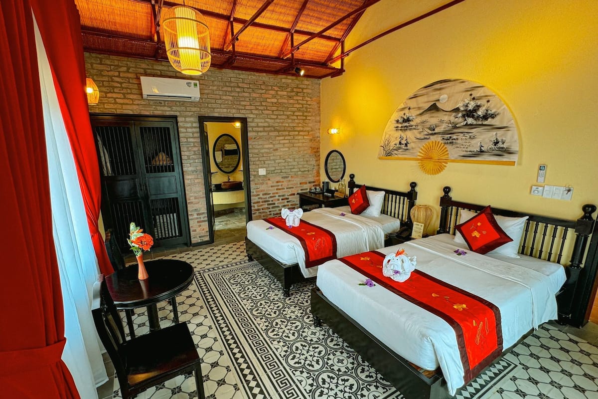 A hotel room with two beds, a small table, a chair, a mirror, and a wall with a painting.