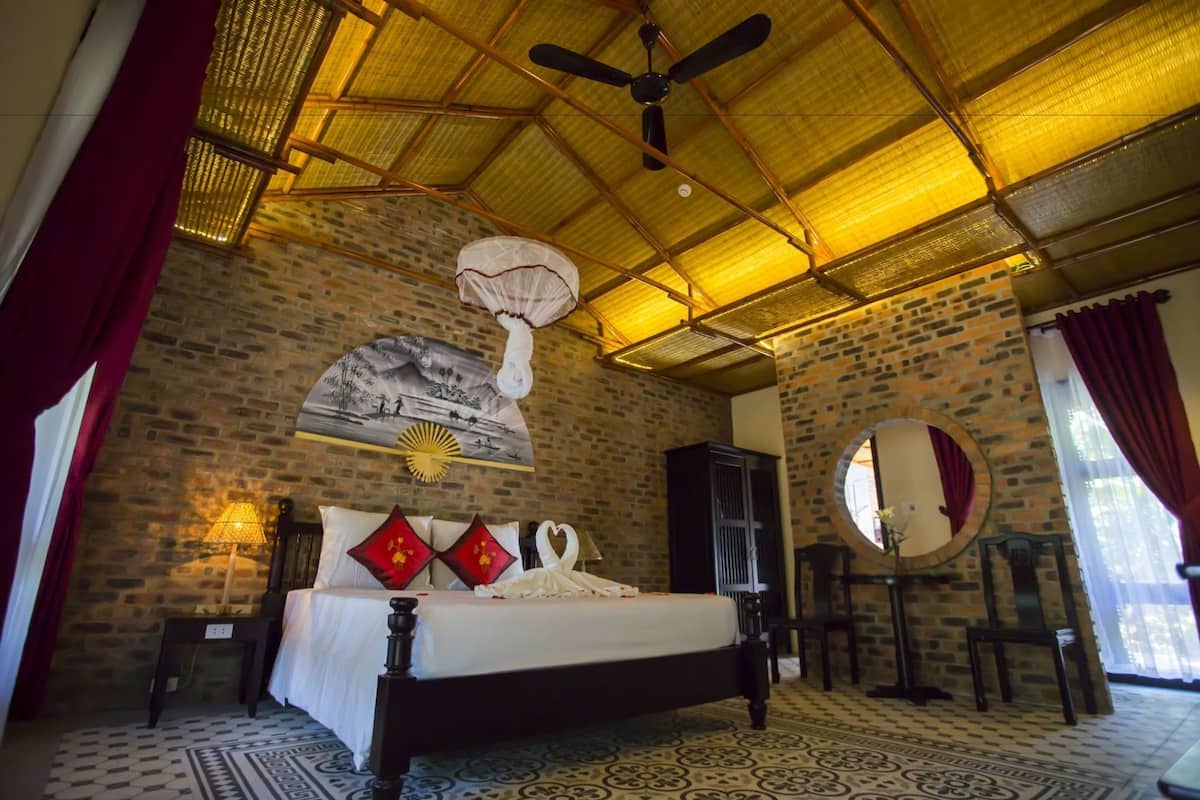 A bedroom with a bed, a ceiling fan, a wall-mounted fan, a mirror, and a patterned floor.