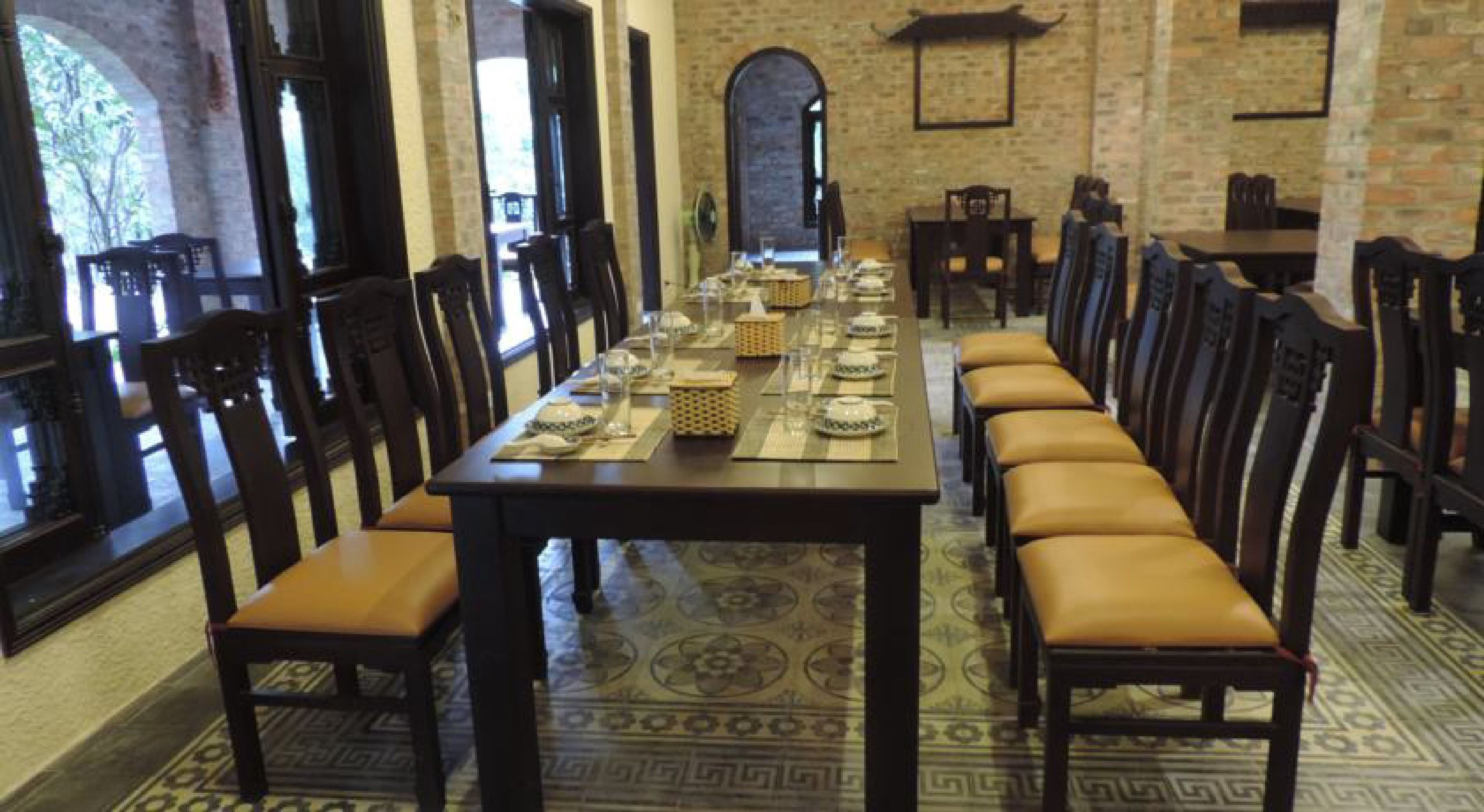 Een lange eettafel gedekt met servies, omringd door stoelen met lederen kussens, in een kamer met bakstenen muren en een kamerbreed tapijt.