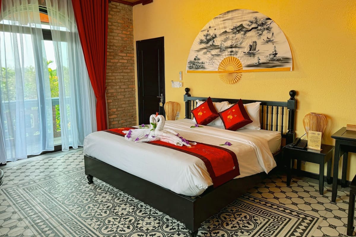 A hotel room with a large bed, a wall-mounted artwork, a wooden headboard, and a patterned floor.
