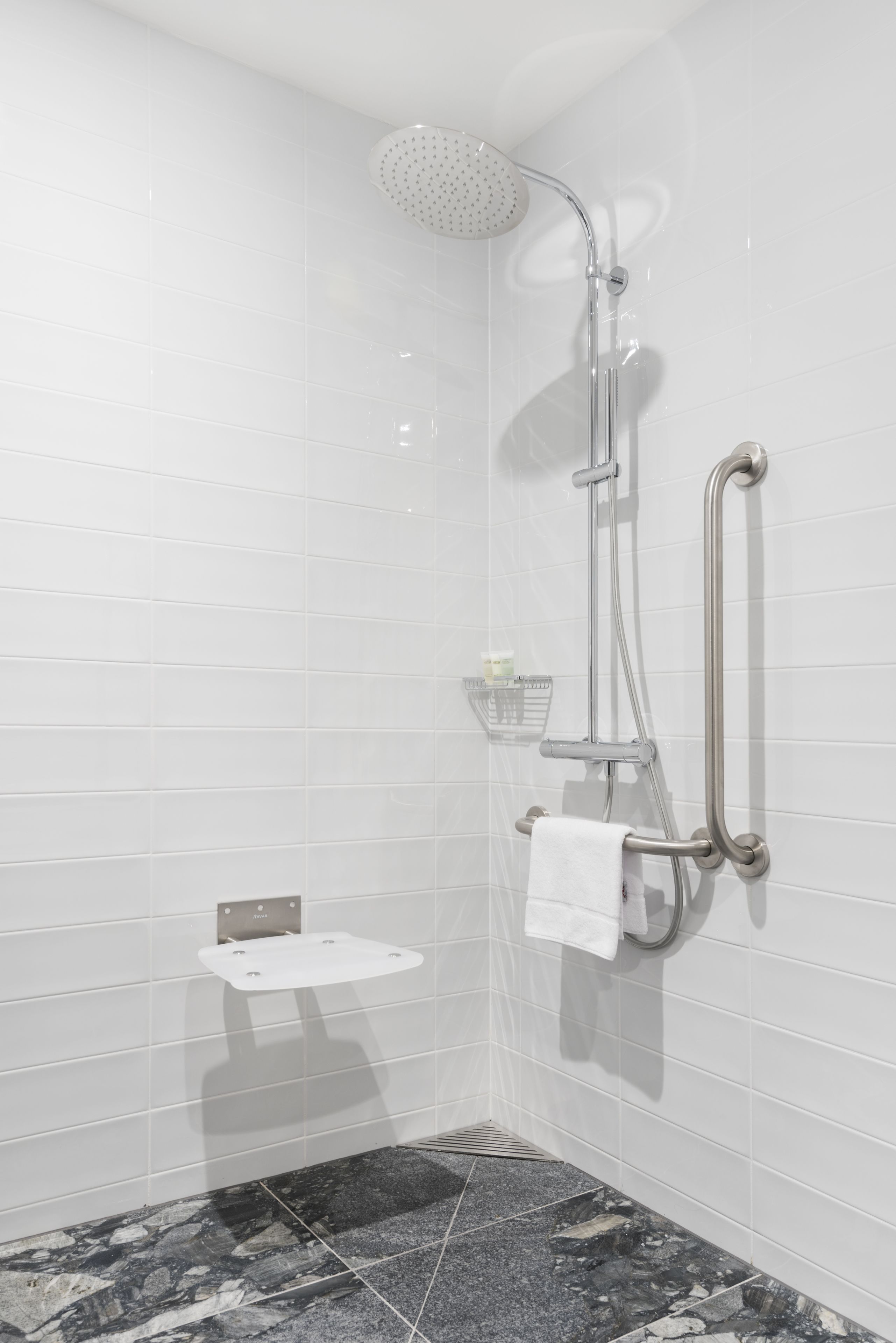 A modern shower with a handheld showerhead, a wall-mounted towel rack, and a small shelf with toiletries.