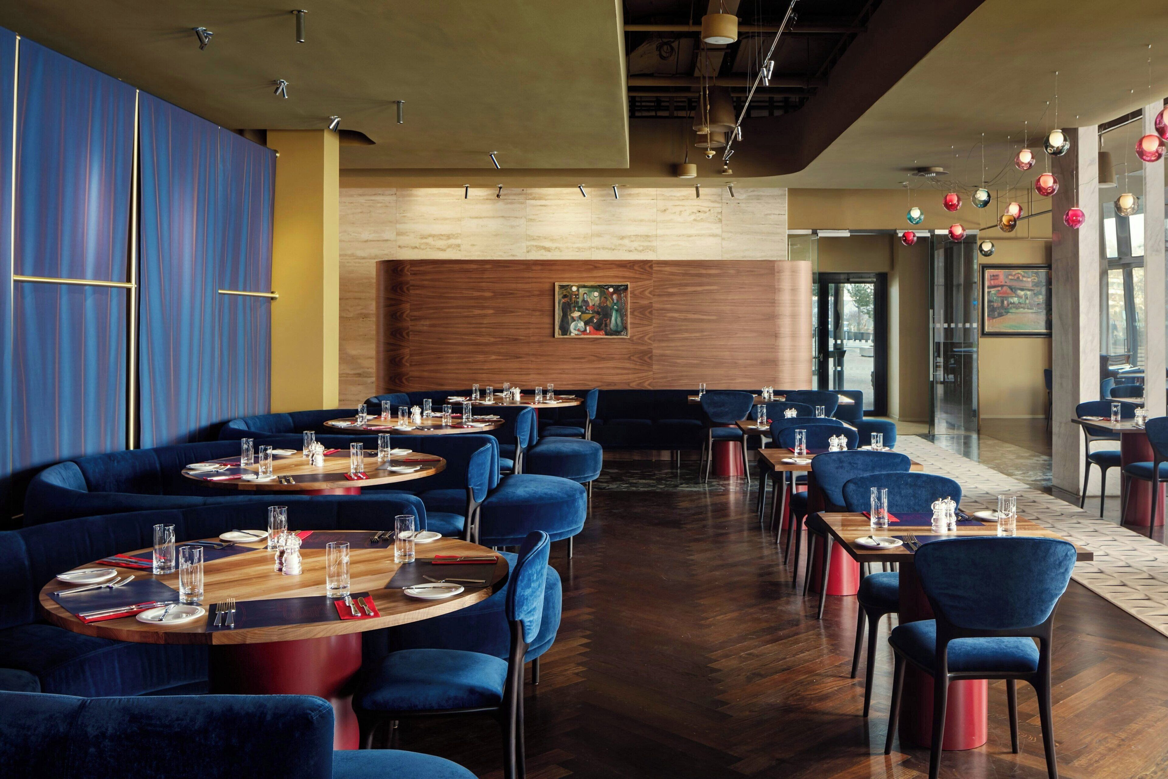 A restaurant with round tables, blue upholstered chairs, and wooden flooring.