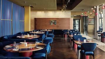 A restaurant with round tables, blue upholstered chairs, and wooden flooring.
