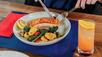 A plate of food with a piece of fish, vegetables, and a glass of drink on a table.
