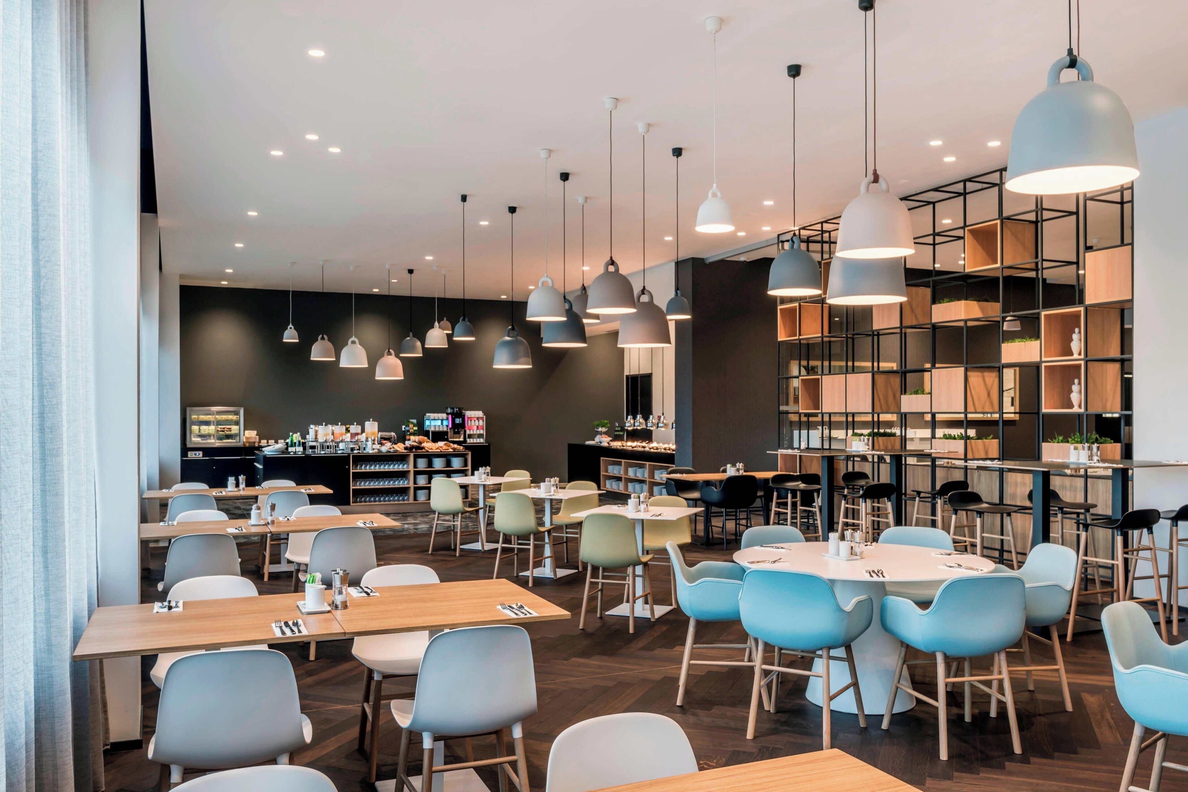 A modern restaurant with multiple dining tables and chairs, pendant lighting, and a bar area with shelves.