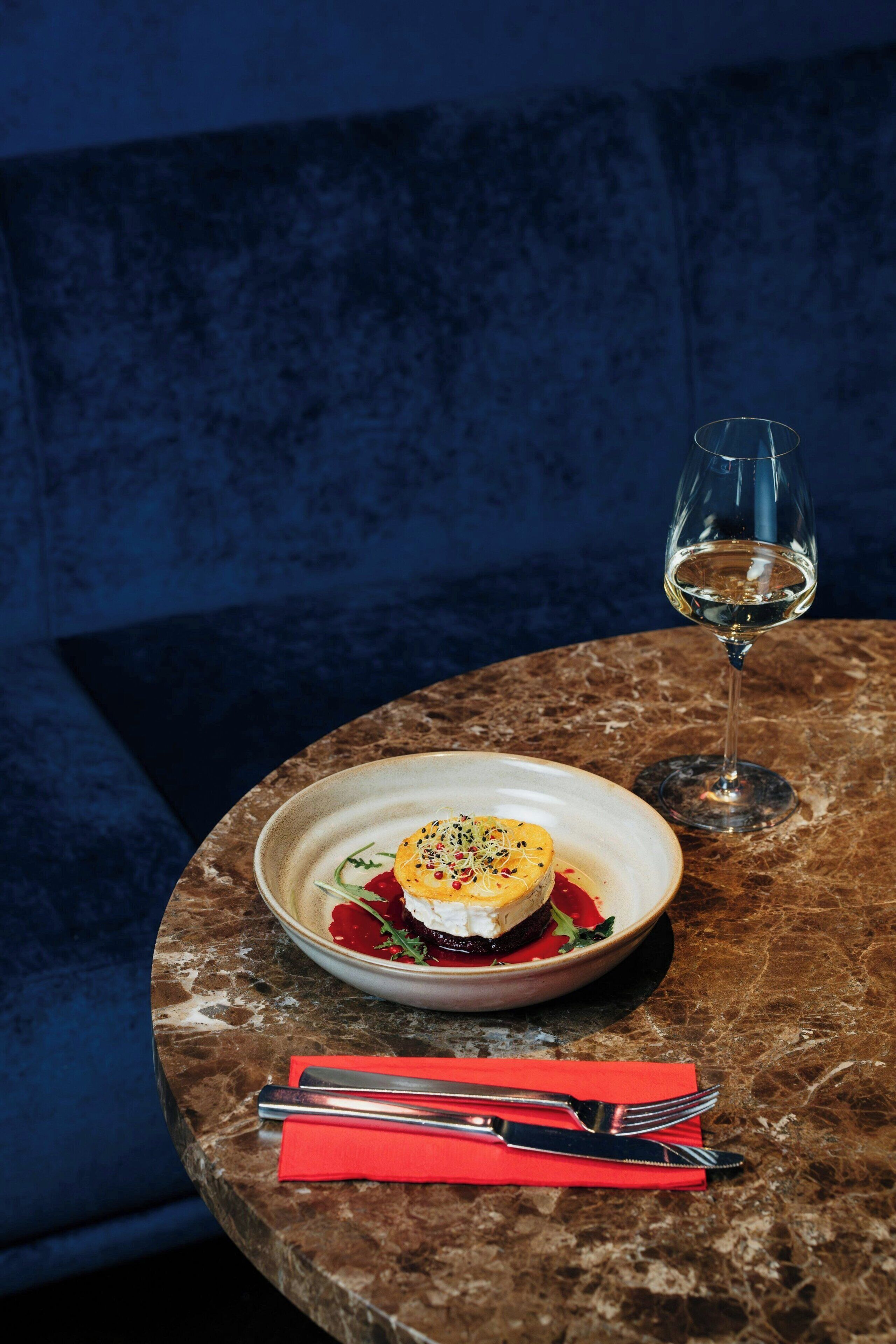 A dining table with a plate of food and a glass of white wine.