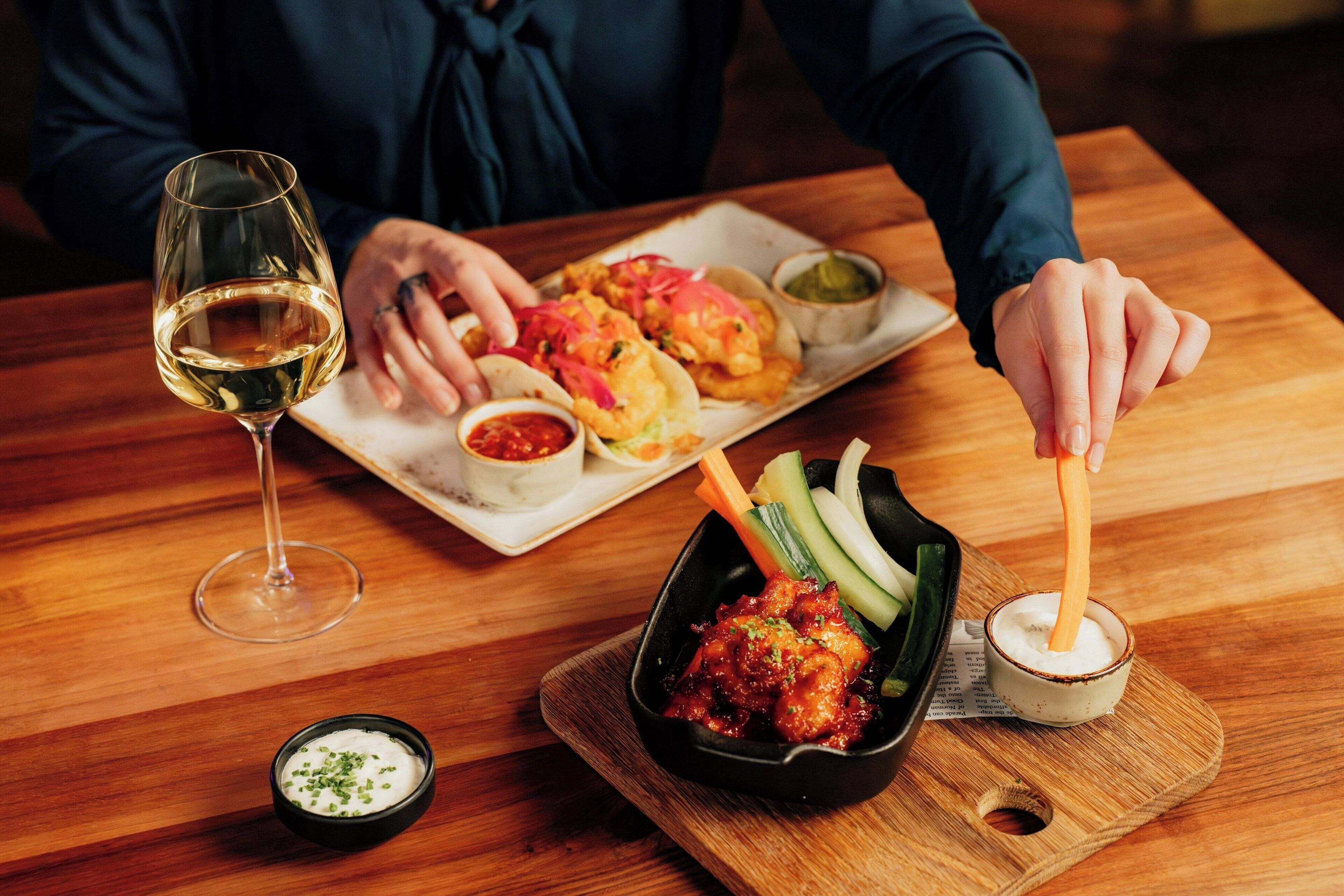 Et spisebord med mad på tallerkenen, et glas vin og en skål med sauce.