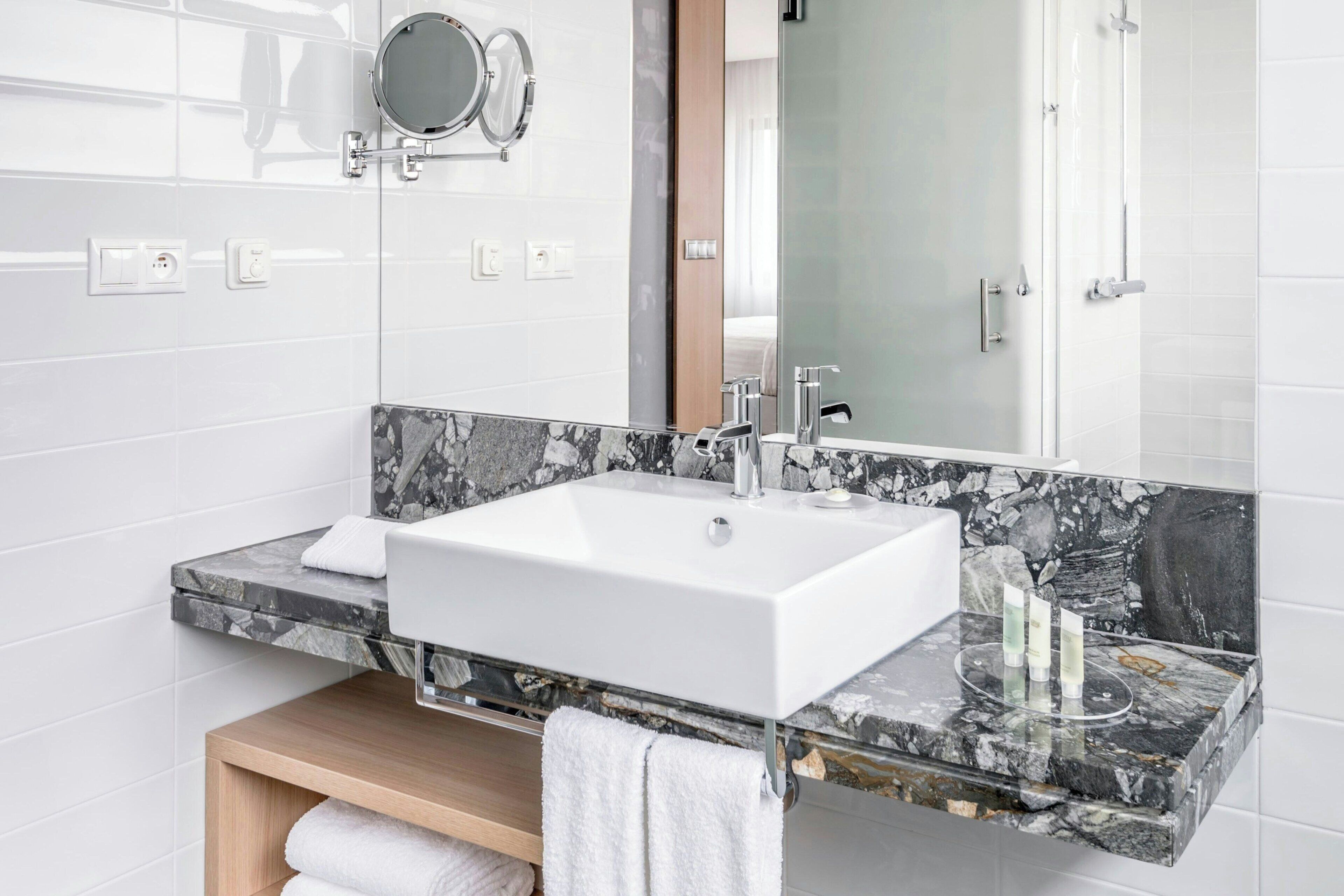 A modern bathroom with a white sink, marble countertop, and a mirror above.