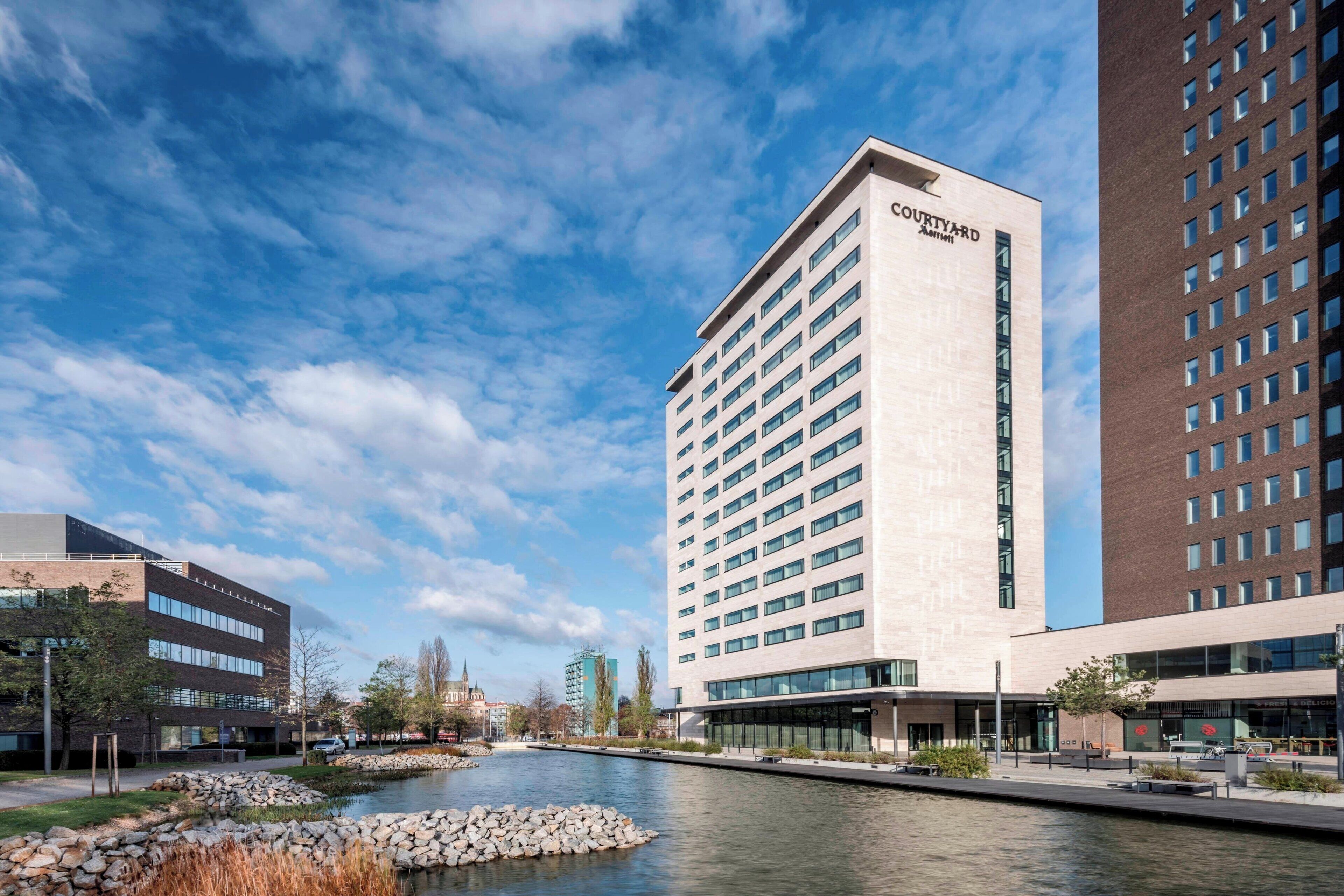 A Courtyard hotel with a modern design, featuring a river and a stone pathway in the foreground.