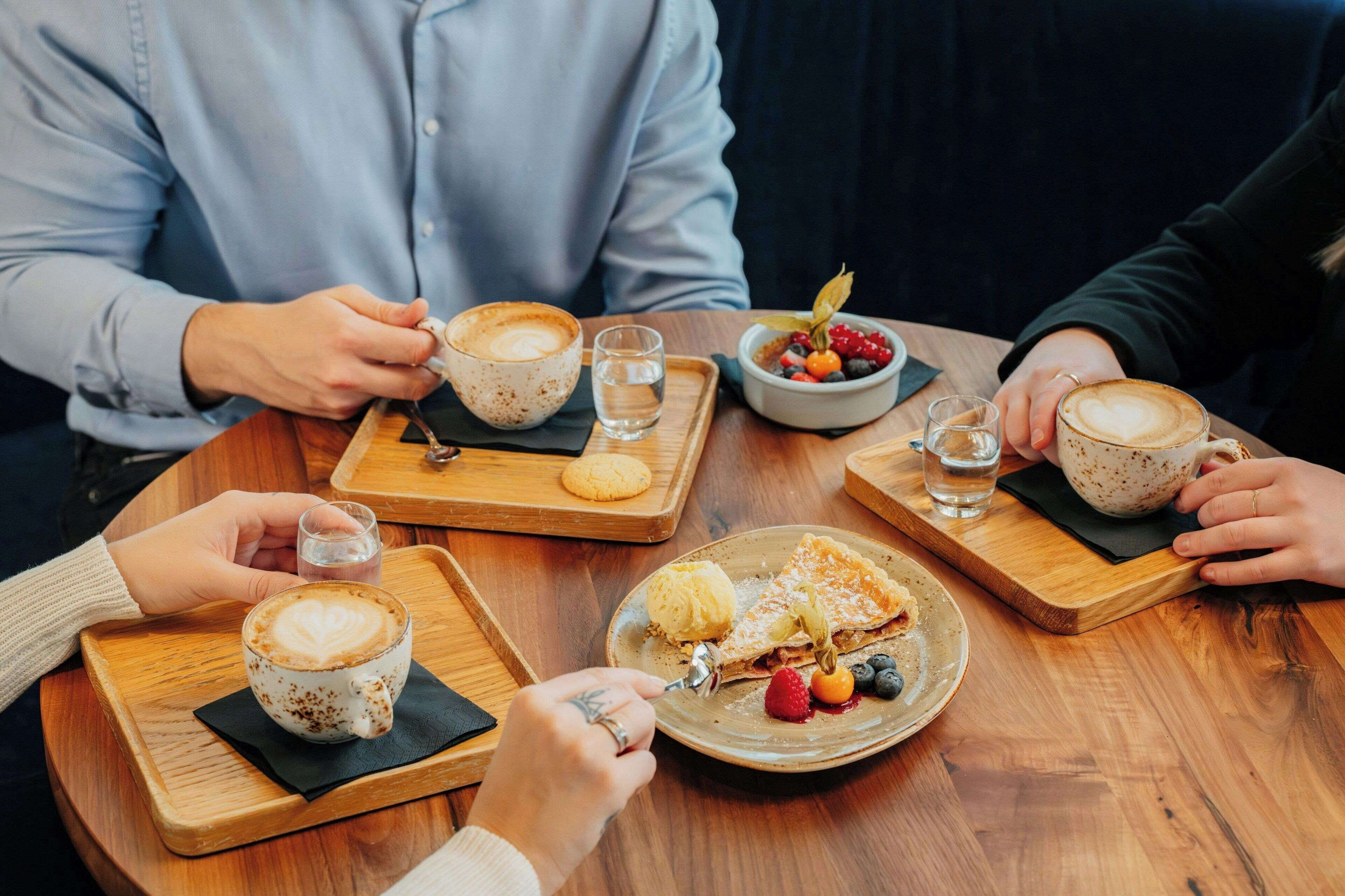 Een houten tafel met een kop koffie, een bord met dessert en een schaal fruit.