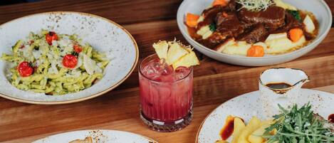 A table with various dishes including pasta, steak, and fries, along with a glass of red drink.