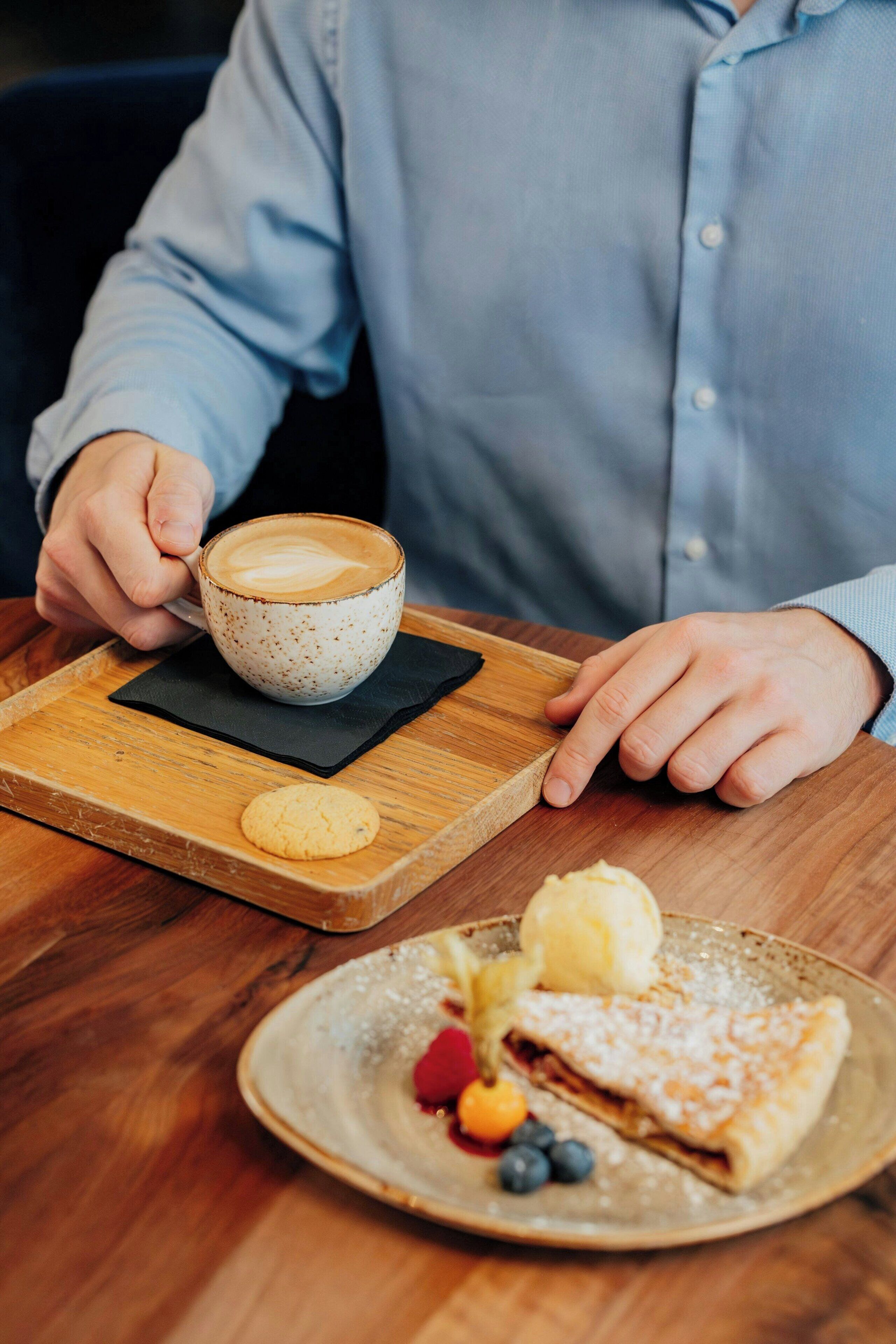 Una persona sosteniendo una taza de café con su platillo sobre una bandeja de madera.