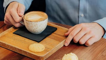 Una persona sosteniendo una taza de café con su platillo sobre una bandeja de madera.