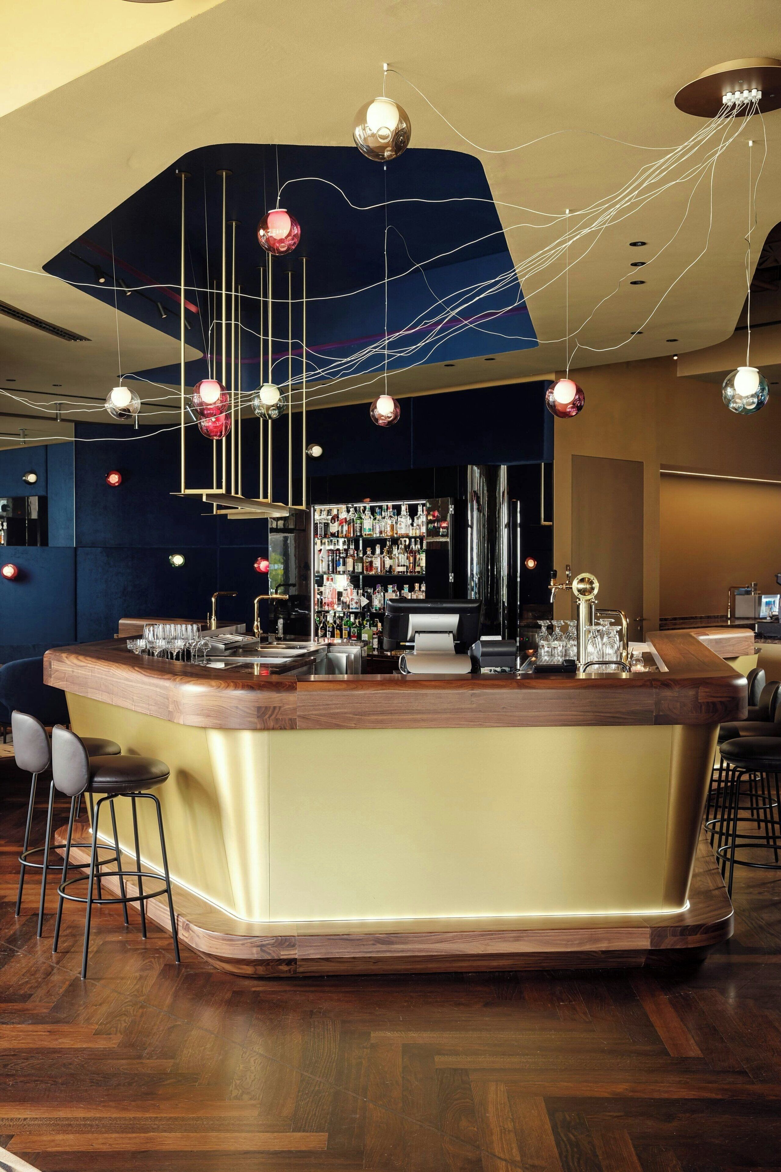 A bar area with a curved counter, stools, and hanging pendant lights.
