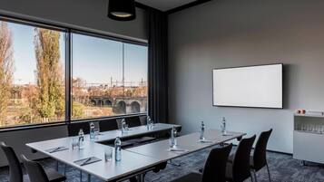 A conference room with a large table, chairs, a projector screen, and a view of a bridge and cityscape through large windows.
