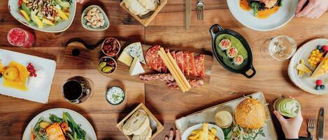 A dining table with various dishes, including salmon, steak, and vegetables, surrounded by people.