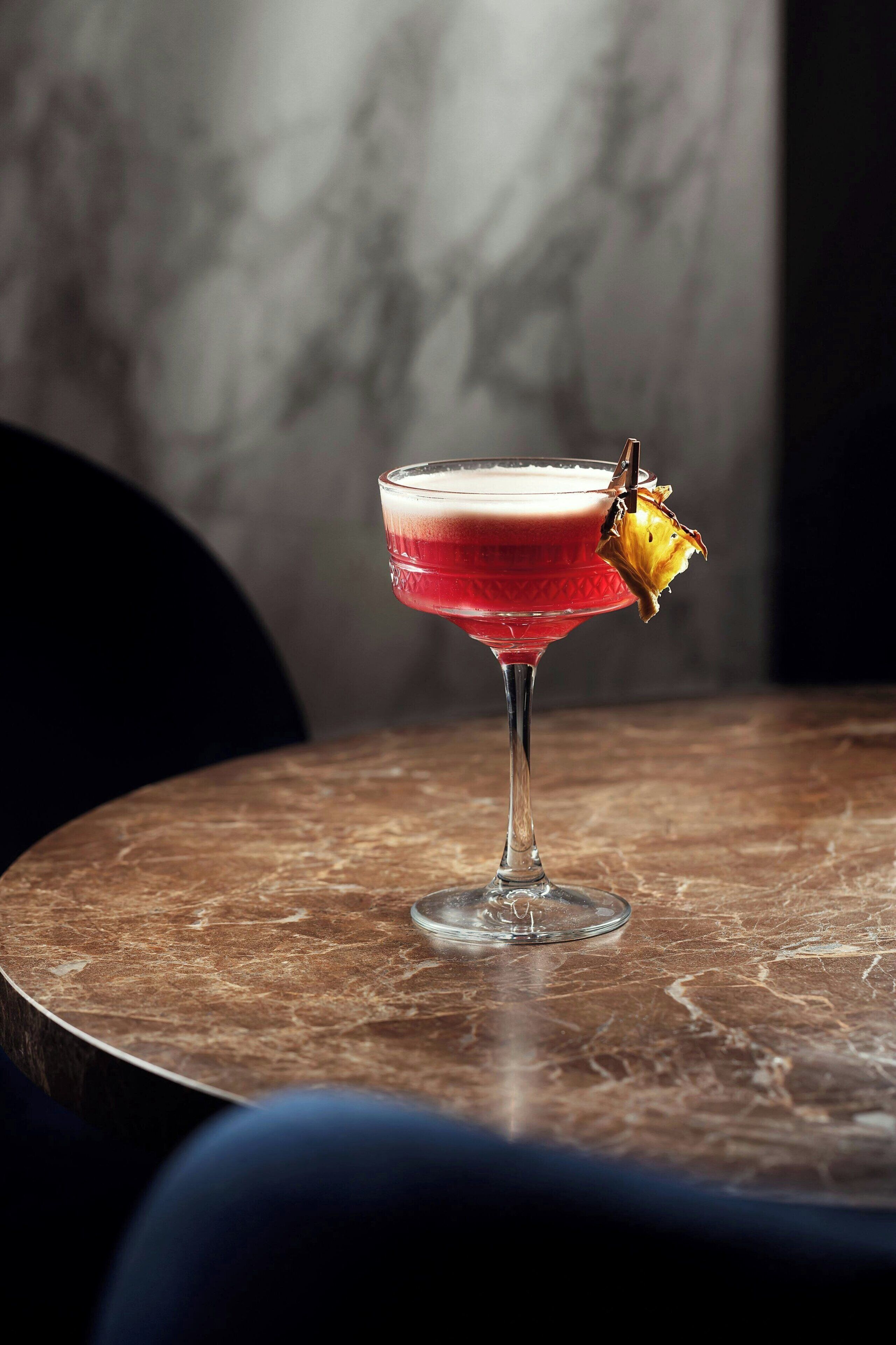 Un cóctel en una copa de martini con una guarnición de piña sobre una mesa de mármol.