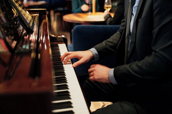 A person playing a grand piano in a room with a round table and blue chairs.