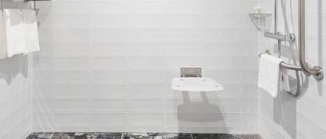 A modern bathroom with white tiled walls, a shower with a handheld showerhead, and a marble floor.