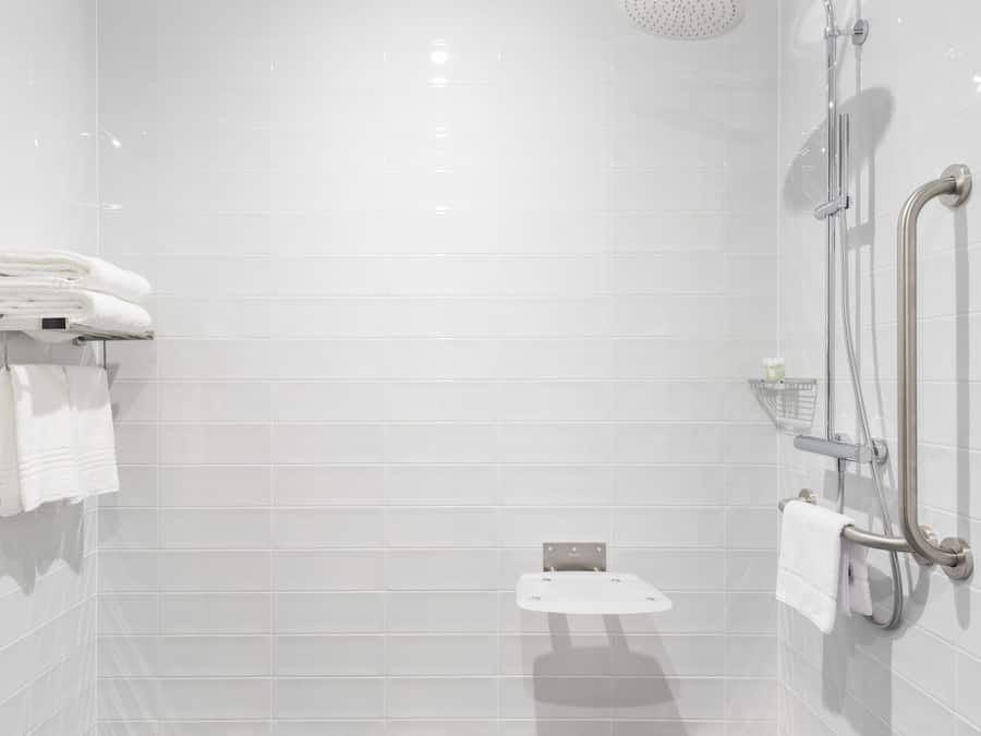 Un baño moderno con paredes de azulejos blancos, una ducha con cabezal de ducha manual y suelo de mármol.