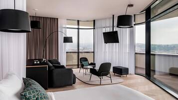 Een moderne hotelkamer met een groot bed, een bureau, een stoel en uitzicht op de stad door grote ramen.