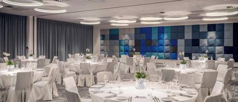 A banquet hall with round tables, white tablecloths, and chairs.