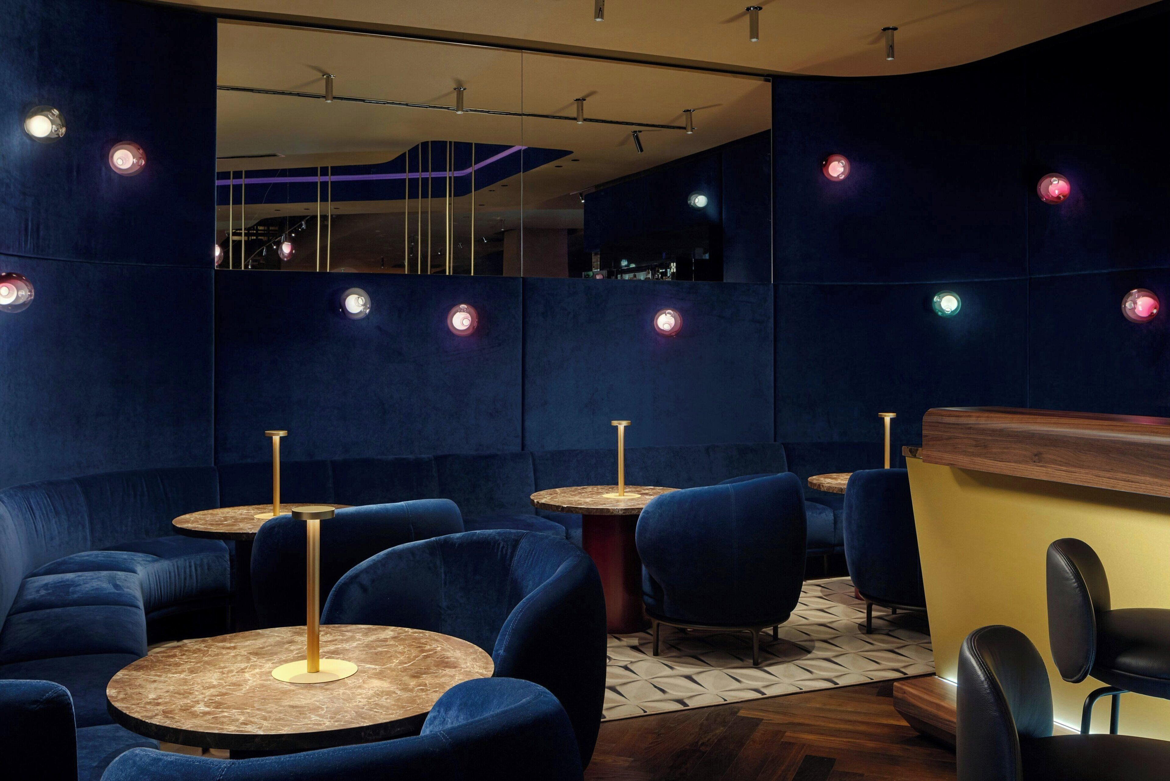 A modern interior with round tables and blue upholstered chairs, a wooden counter, and a patterned floor.