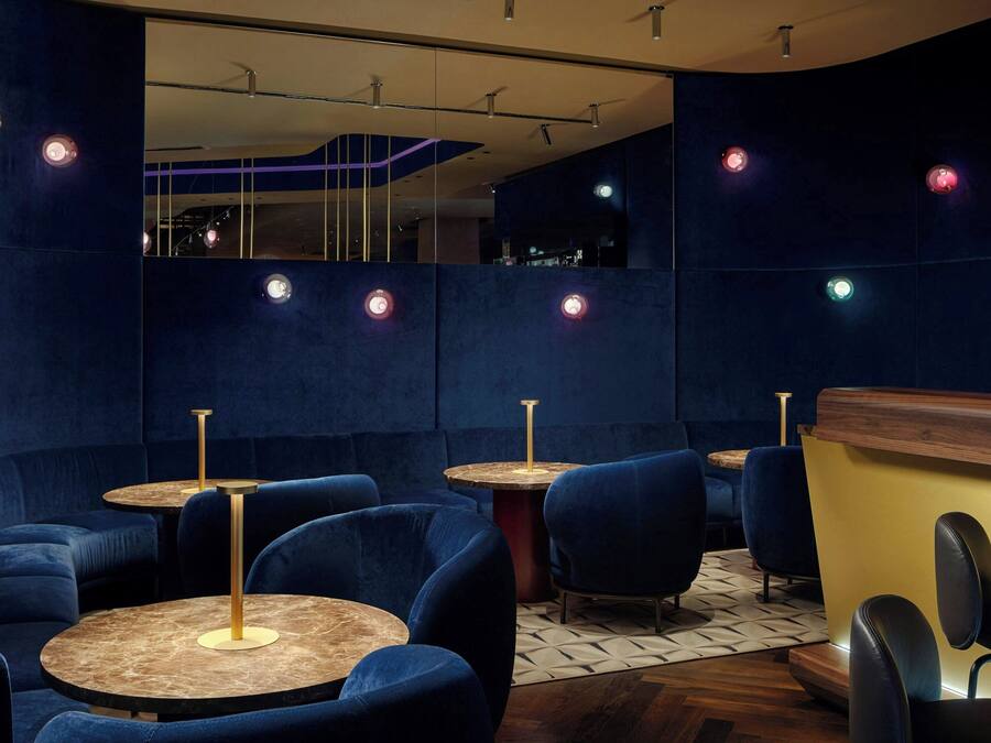 A modern interior with round tables and blue upholstered chairs, a wooden counter, and a patterned floor.