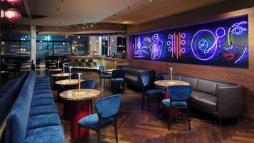 A modern lounge area with seating, a bar, and a neon art installation.