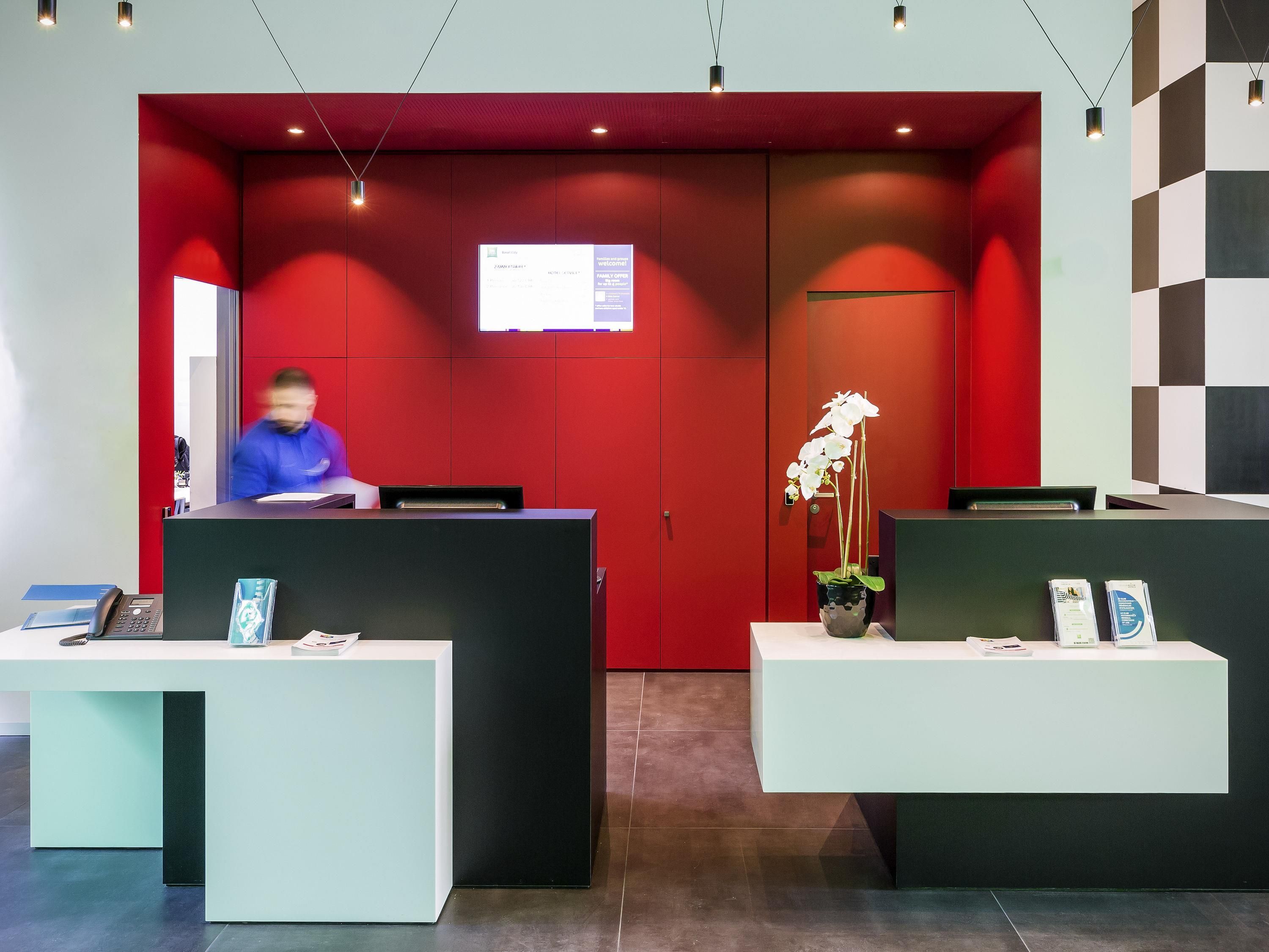 A reception area with two reception desks, a red wall, a digital screen, and a potted orchid.