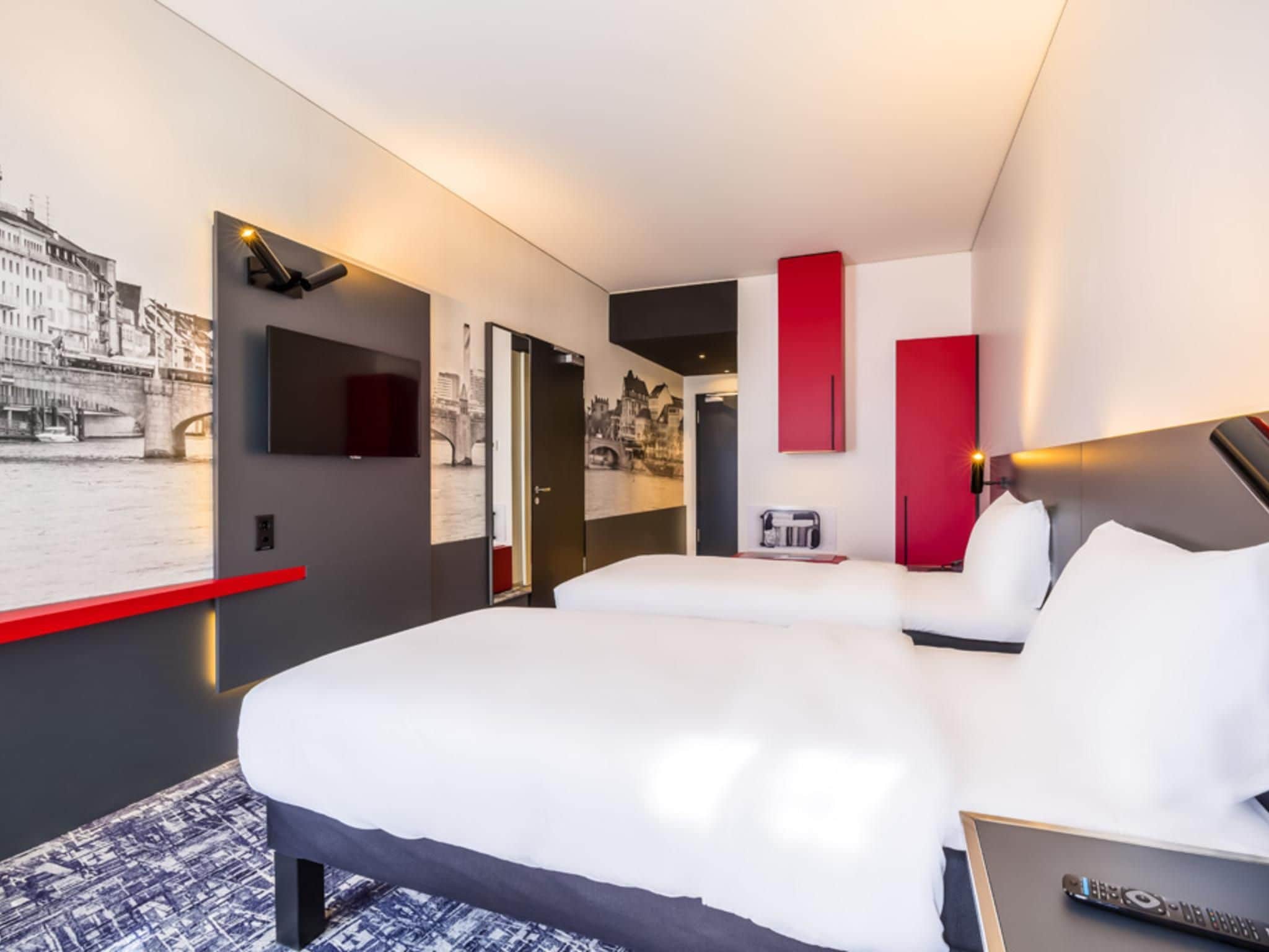 A modern hotel room with a large bed, a flat-screen TV, and a cityscape mural on the wall.