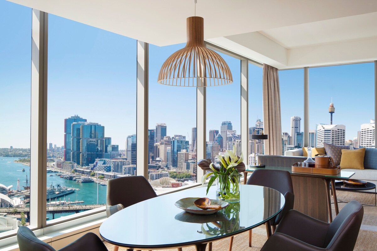 Un comedor moderno con una mesa de vidrio, sillas y vista a la ciudad.