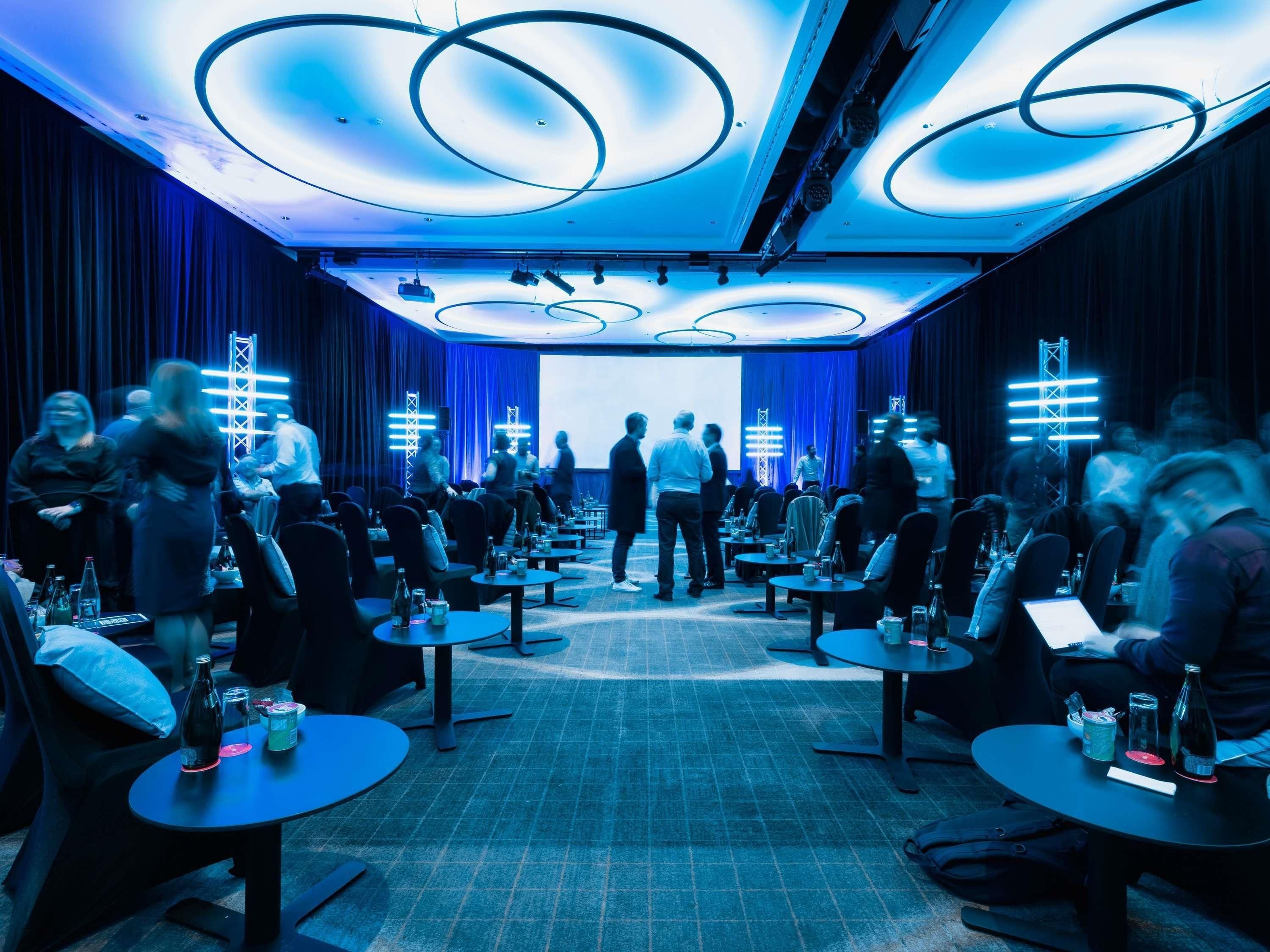 A conference room with round tables, chairs, and a stage at the front.