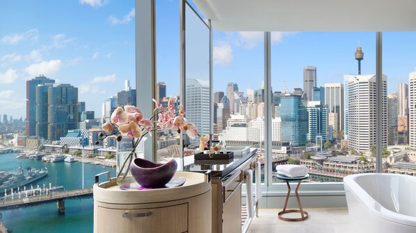 A modern bathroom with a city view, a bathtub, and a vanity with a vase of orchids.