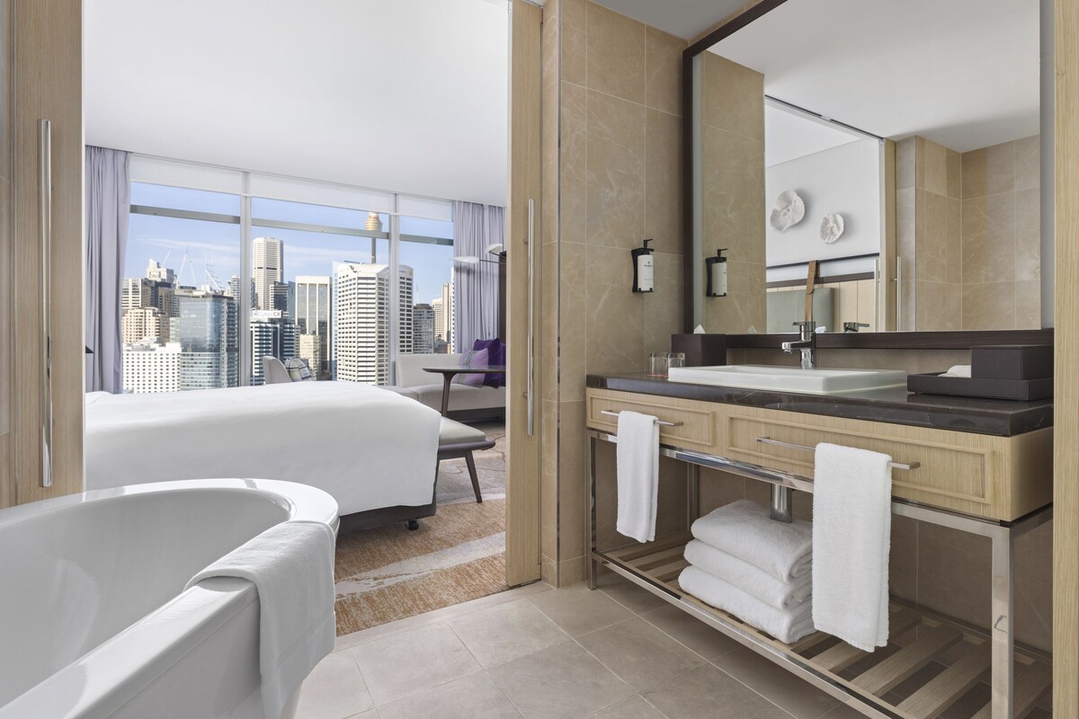 Una habitación de hotel moderna con una cama grande, una bañera, un tocador con espejo y vistas a la ciudad.