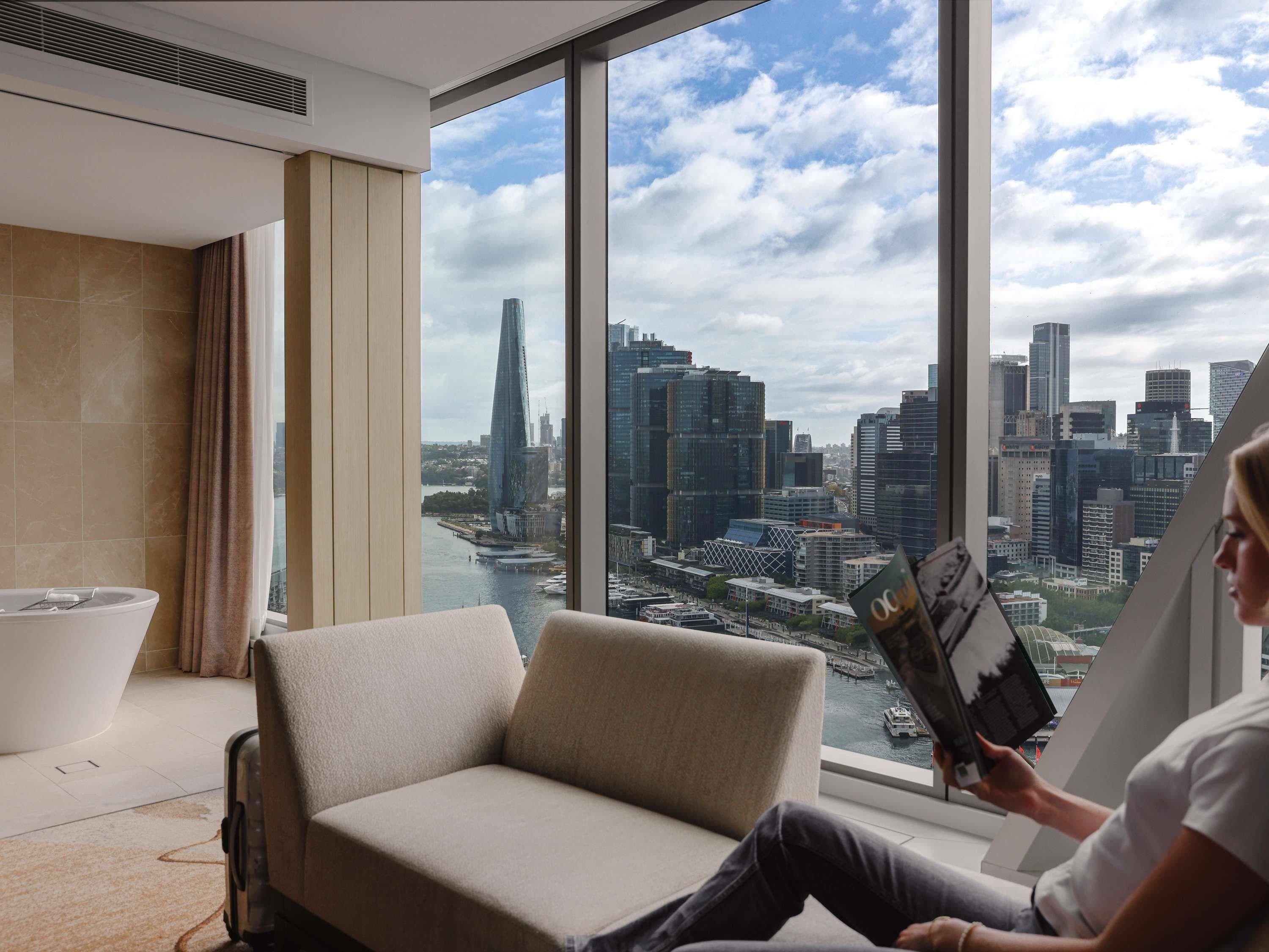 A modern room with a large window, a sofa, and a person reading a magazine.